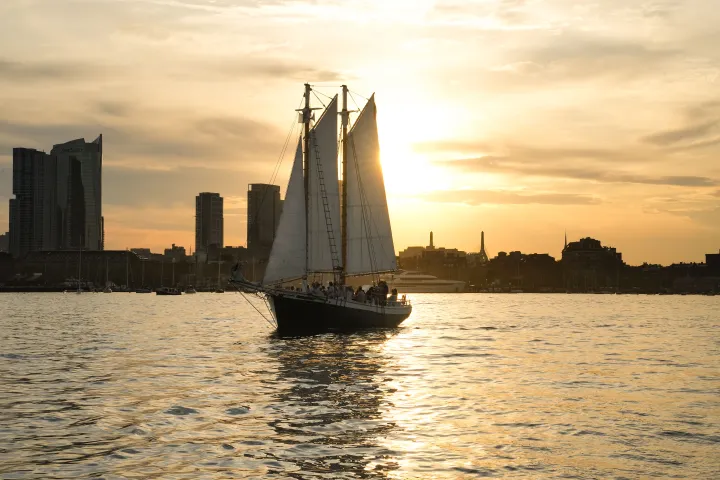 Silhouette of a sailboat on water against a city skyline at sunset.