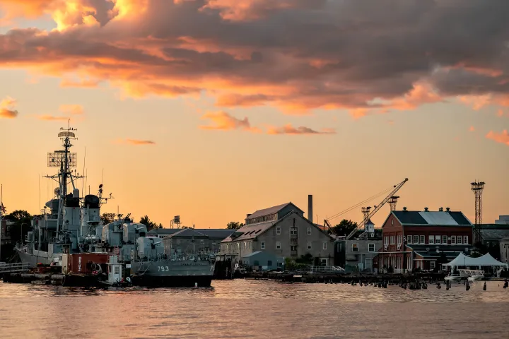 Harbor with ships and buildings under a sunset sky with clouds.