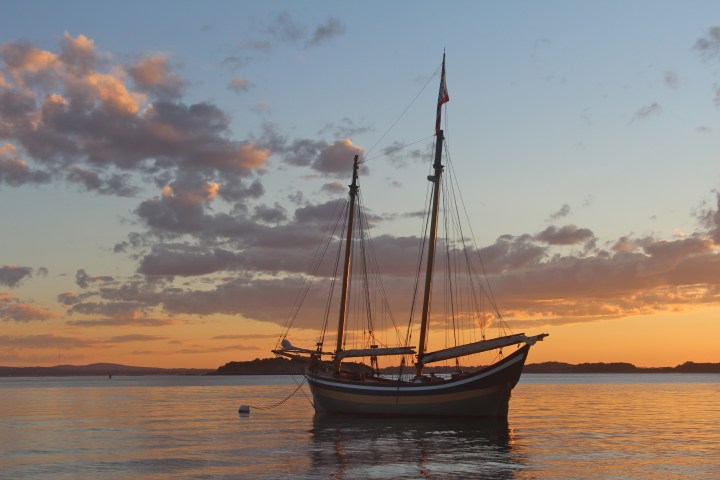 Sailing ship on calm water at sunset with colorful sky and clouds.