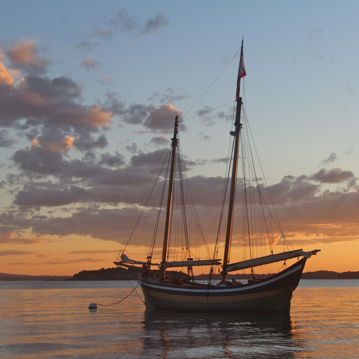 Sailing ship on calm water at sunset with colorful sky and clouds.
