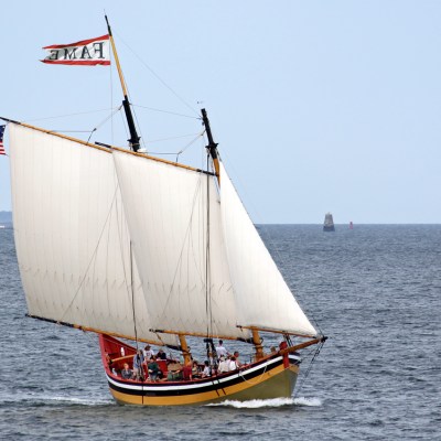 A sailing ship with two sails and American flag on open sea.
