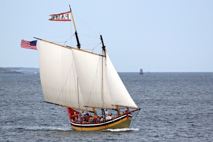 A sailing ship with two sails and American flag on open sea.