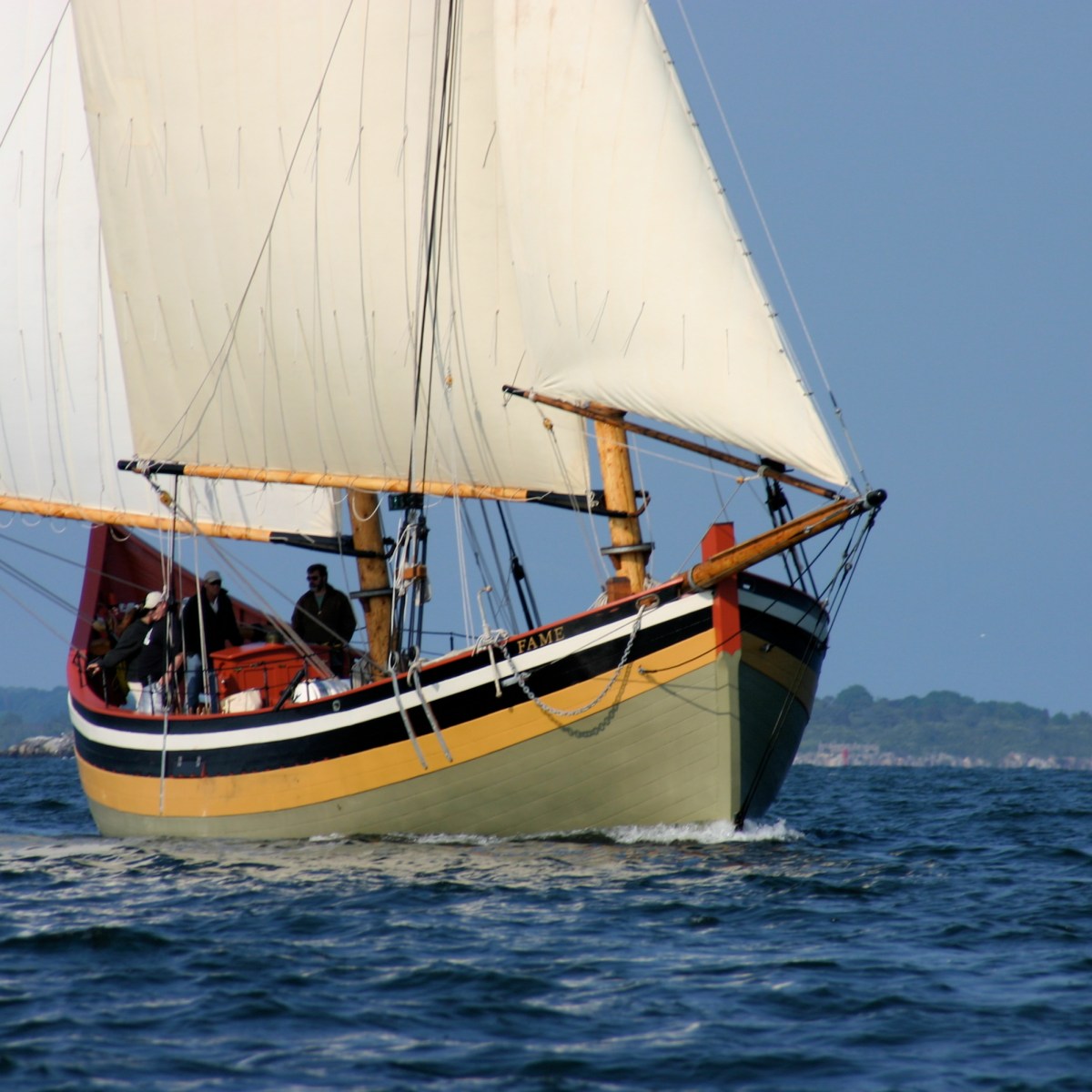 Sailing ship with cream sails on blue sea under clear sky.