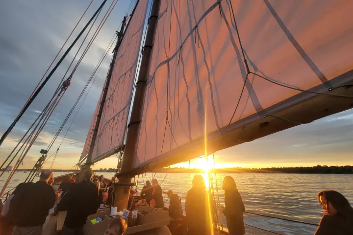 Sunset view aboard a sailboat with people and large sails.