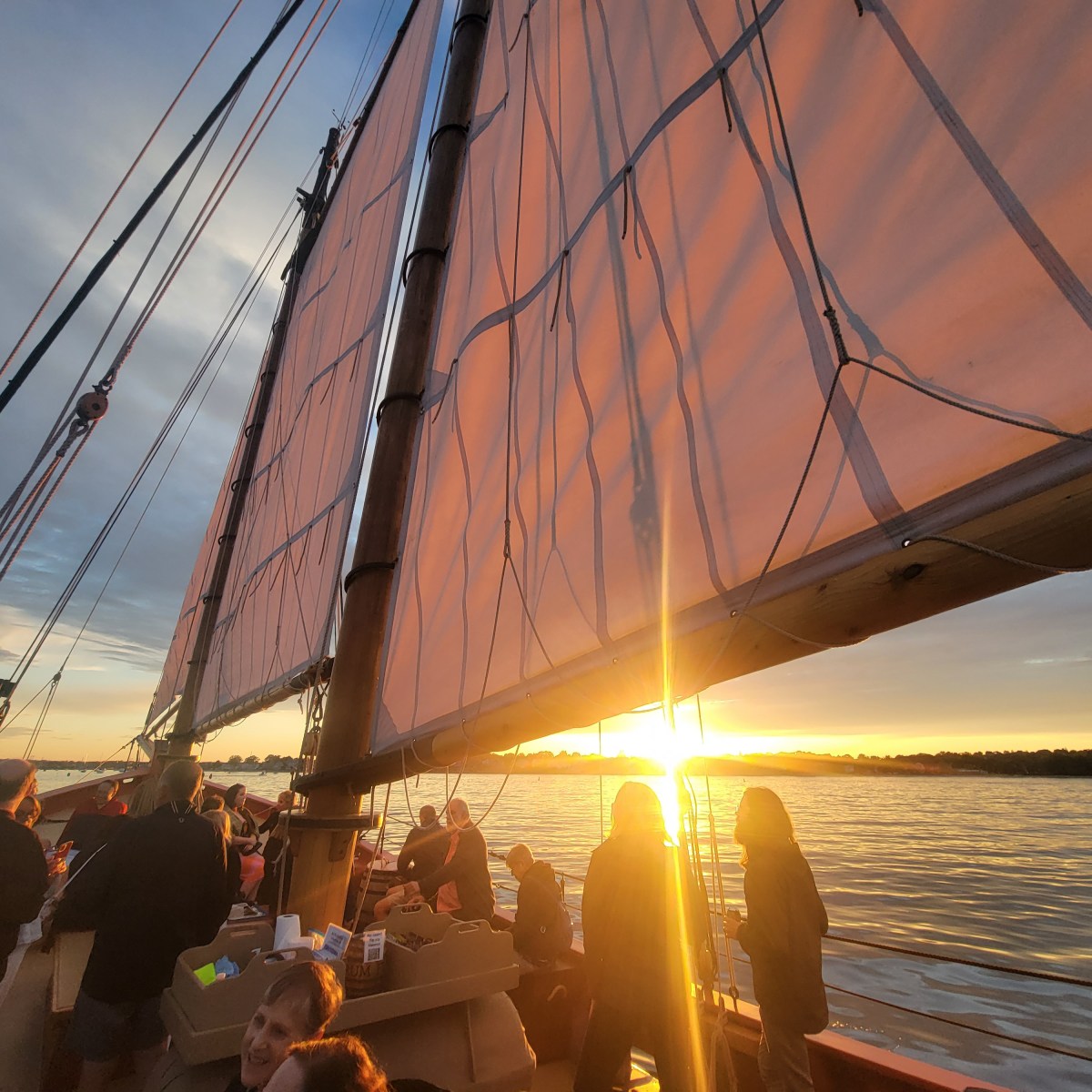 Sunset view aboard a sailboat with people and large sails.
