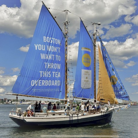 Sailboat with blue sails featuring an advertisement on a sunny day with cloudy sky.