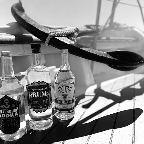 Three liquor bottles on a wooden deck near a large ship's anchor.