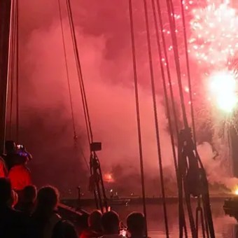 People on a boat watch colorful fireworks illuminate the night sky.