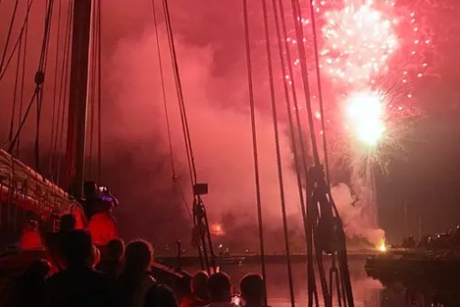 People on a boat watch colorful fireworks illuminate the night sky.