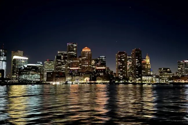 City skyline at night with lit buildings reflecting on the water.