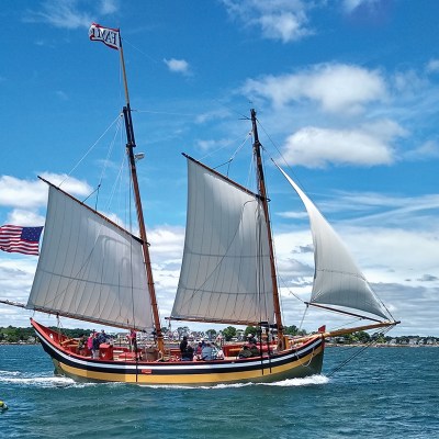 Sailing ship with American flag on blue water under partly cloudy sky.