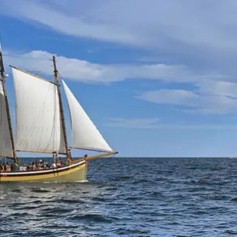 A sailboat with two sails and flags on a large body of water under a blue sky with clouds.