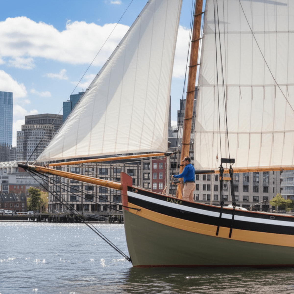Large sailboat on a river with city skyline in the background.